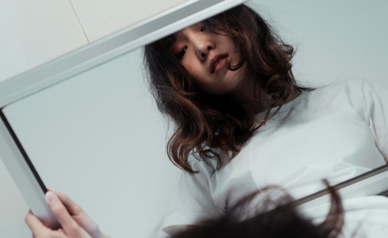 거울을 보며 고민하는 여성의 모습, 옆에는 성형 관련 정보들이 놓여 있다.